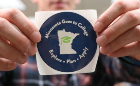 student holding MN goes to college sticker 
